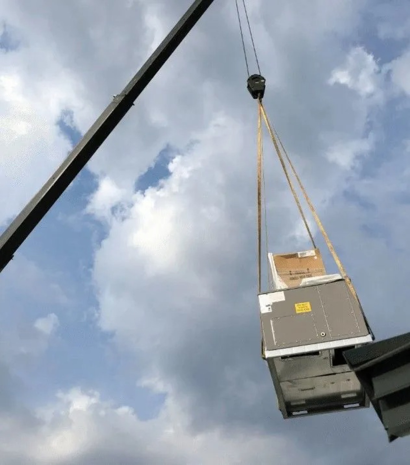 Rooftop air handler being crane-lifted into place against a dramatic sky